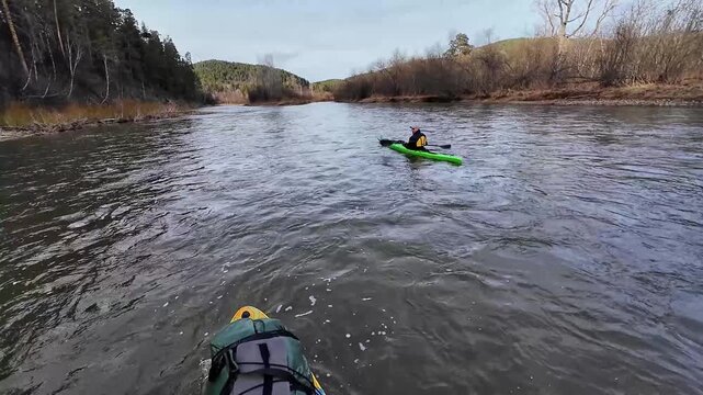 White kayaker cruising open river channel two kayakers cut across broad water, gentle swells and forested banks, bow equipment visible, overcast light and calm exploration vibe.