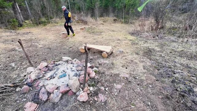 Scout examines campfire location. Hiker observes fire area while carefully navigating meadow. Adventurer strolls across countryside inspecting designated camping spot thoroughly