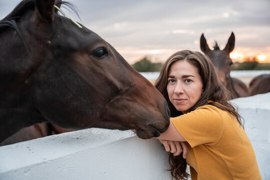 Woman resting by white fence with horse at sunset ranch