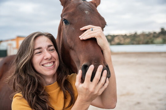 Smiling woman hugging horse at outdoor riding arena