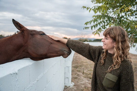 Woman petting horse over white fence on a quiet farm