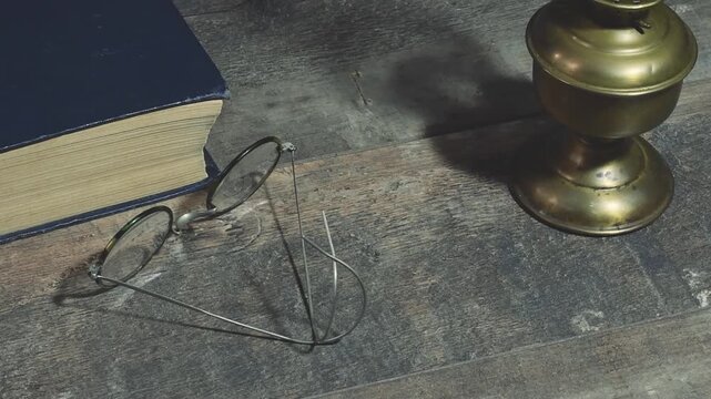 Man picks up antique pocket watch from table with lamp, book, and glasses