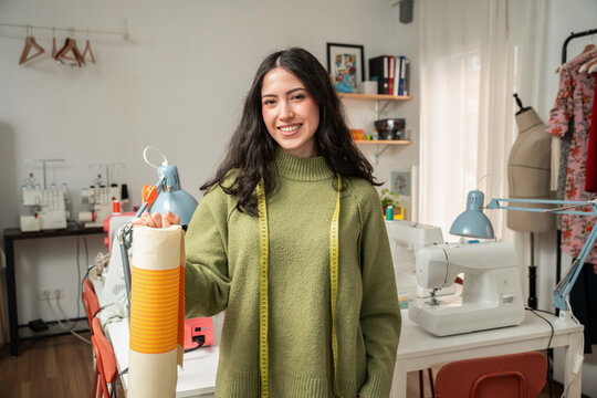 Portrait of young woman designer in fashion atelier looking at camera