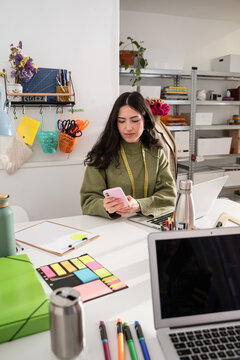 Woman using smartphone at fashion atelier worktable