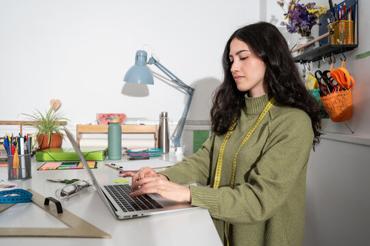 Woman designer working on laptop in fashion atelier studio