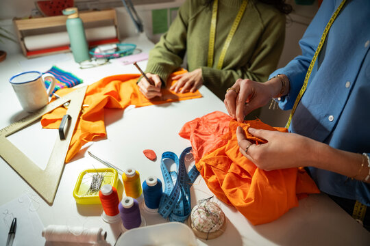 Woman tailor hand sew orange dress in fashion atelier