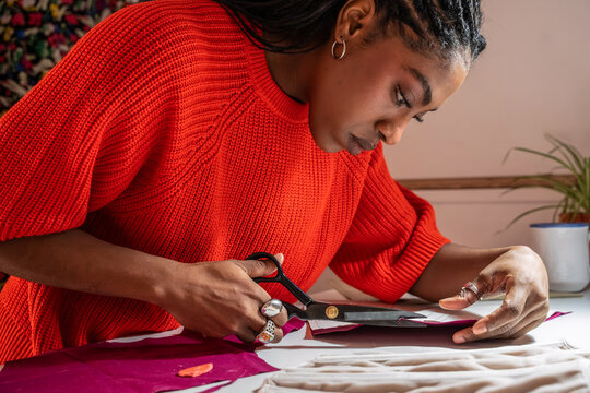 Focused black colombian woman cuts fabric at a fashion atelier table