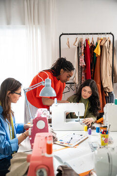 Teacher guiding students in sewing workshop with machine