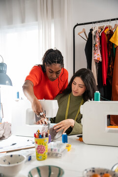 Teacher guiding student at sewing workshop with machine
