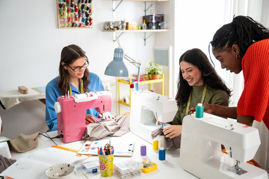 Teacher guiding students in sewing workshop with machines
