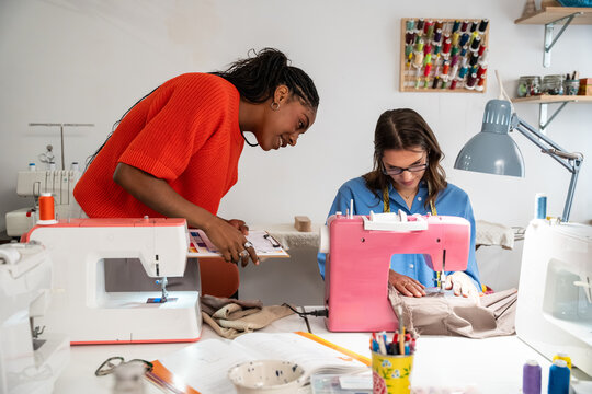Teacher guiding student at sewing workshop with machines