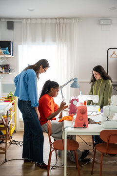 Multiethnic women sewing garment in bright fashion atelier