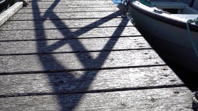 Weathered wooden dock plank texture with geometric shadow pattern from railing over marina water, sunlight highlighting weathered pier and railing contrast, rustic wooden plank boardwalk reflecting