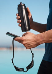 Fototapeta premium Bottle, swimmer and hands of man with phone outdoor for texting, networking or contact at practice. Typing, fitness and athlete with cellphone for social media on mobile app at competition training.