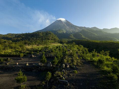 Aerial view of Bunker Kaliadem Merapi with the smoking peak of Mount Merapi volcano and lush green forests in Kecamatan Pakem, Daerah Istimewa Yogya, Indonesia.