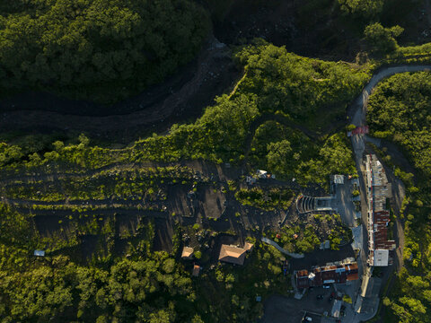 Aerial view of Bunker Kaliadem Merapi surrounded by lush green forests and volcanic terrain under warm sunlight in Kecamatan Pakem, Daerah Istimewa Yogya, Indonesia.