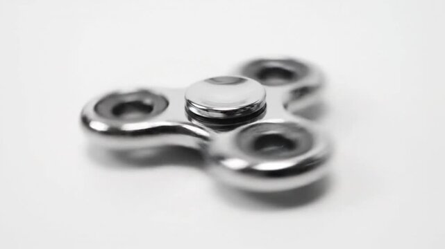 Close-up of a silver fidget spinner spinning rapidly on a white background, generating white noise sound