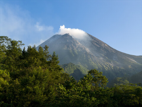 Aerial view of the majestic Mount Merapi volcano with smoke rising from its crater above lush green forests Kecamatan Pakem, Daerah Istimewa Yogya, Indonesia.