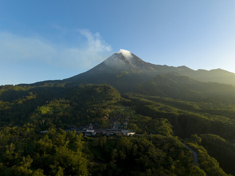 Aerial view of Bunker Kaliadem Merapi and the smoking peak of Mount Merapi surrounded by dense tropical forests in Kecamatan Pakem, Daerah Istimewa Yogya, Indonesia.