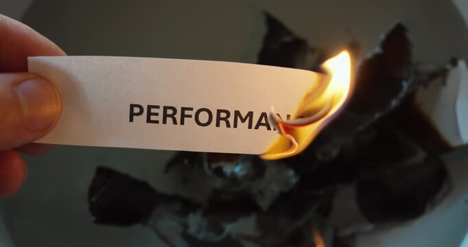 Close-up of paper labeled &ldquo;performance&rdquo; being burned, symbolizing loss, decline, or elimination of productivity and efficiency.