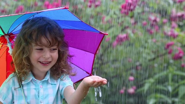 Child having fun under rain in spring park outdoors. Slow motion