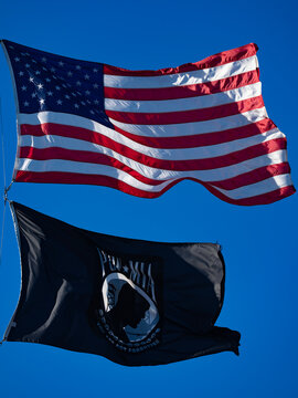 American flag waves beside POW banner. Patriotic American symbol honors veterans. United American heritage supports freedom. National American pride protects tradition.