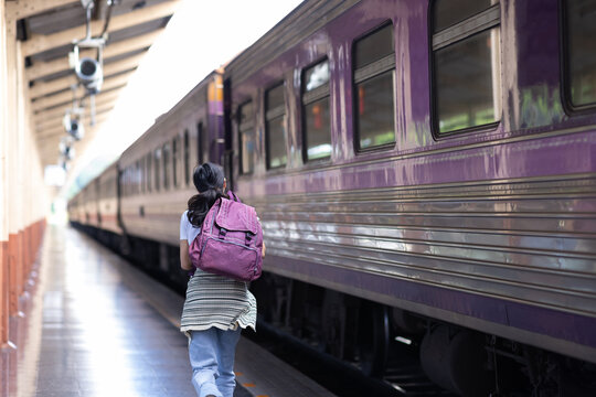 Woman traveler carrying a backpack running alongside a moving train on a station platform, highlighting concepts of travel, urgency, and transportation.