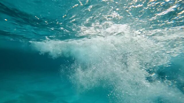 Underwater perspective of a breaking wave in a turquoise pool with sunlight reflections