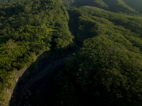 Aerial view of the lush green forest and deep volcanic ravine near Bunker Kaliadem Merapi under soft sunlight Kecamatan Pakem, Daerah Istimewa Yogya, Indonesia.