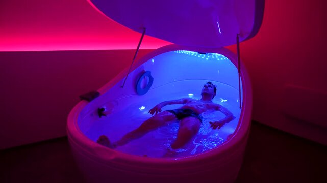 Caucasian man floating in hyper-saline floatation therapy pod, indoor, static shot, medium shot