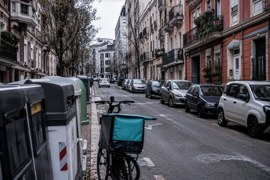 Delivery bike stands near recycling bins on a quiet European street, overcast cinematic look for urban mobility, sustainability and local delivery advertising.