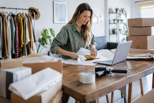 Small business owner packs online fashion orders with boxes, laptop, and tissue paper, bright cinematic e-commerce scene for startup marketing and retail ads