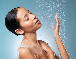 Naklejka premium Water drops, skincare and shower with woman in studio for beauty, hydration cosmetics and cleaning. Self care, splash and moisture with female person on blue background for soap and dermatology