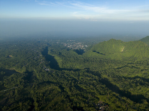 Aerial view of the lush green forest surrounding Bunker Kaliadem Merapi with deep valleys and hills under a clear sky in Kecamatan Pakem, Daerah Istimewa Yogya, Indonesia.