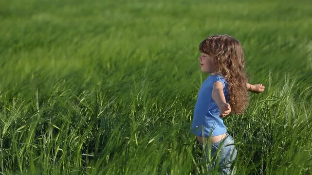 Happy child having fun in green spring wheat field. outdoors. Slow motion