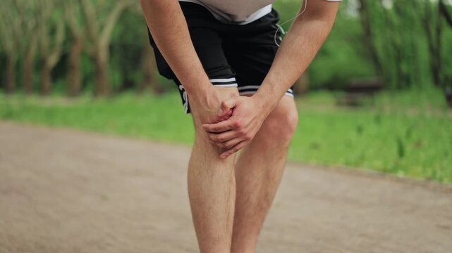 Close up of sportsman touching leg due to acute knee pain during workout outdoors. Concept of ligament strain, meniscus injury, inflammation or joint problems during morning training in park.
