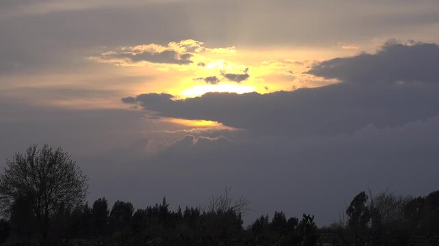 Sunset timelapse clouds above French countryside plain, storm builds as sunlight fades. Dusk fast motion shows thick overcast over rural woodland lowlands, amber glow slips away.