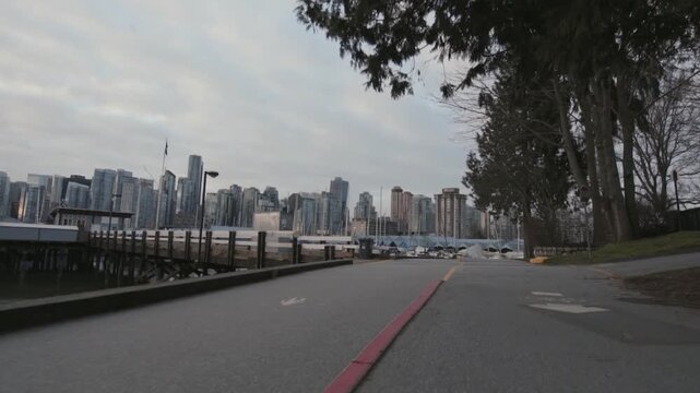 Smooth gliding motion along a paved pathway beside a serene marina with downtown Vancouver cityscape as backdrop under cloudy sky.