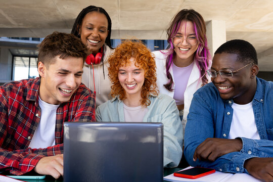 Happy students watching laptop at university campus: multi-ethnic group project