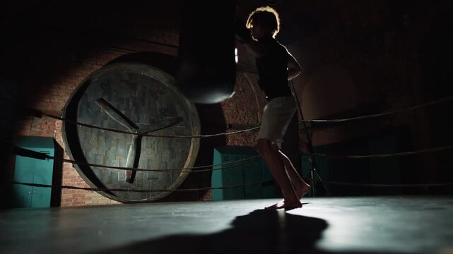 Energy of sport, professional fighter training in boxing ring hitting punch bag. Cinematic slow motion shot with brawny male silhouette doing arms punches, fight in darkness with invisible enemy