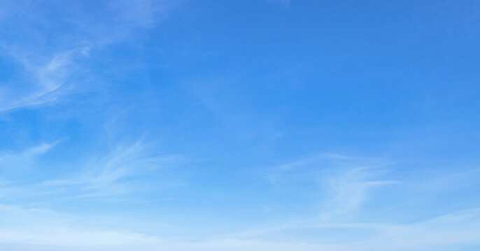 Clear blue sky with wispy clouds drifting gently. Soft gradients from deep to pale blue dominate the frame