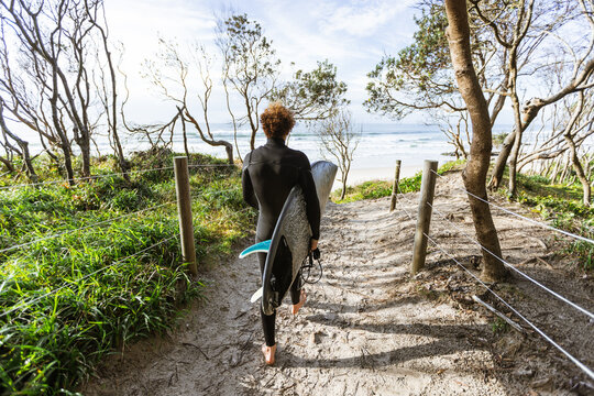 Surfer walking with surfboard on sandy path towards the ocean