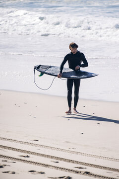 Surfer in wetsuit walking along beach with surfboard