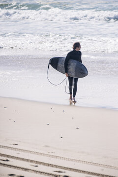 Surfer walking on beach carrying surfboard looking at ocean