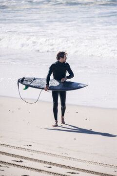 Surfer in wetsuit walking along beach with surfboard