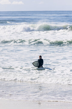 Surfer standing in ocean surf with surfboard