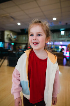Little girl holding an orange ball at bowling in indoor alley