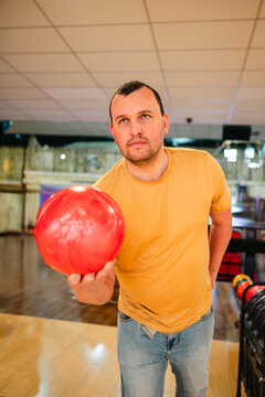 Man at bowling holding red ball in indoor alley