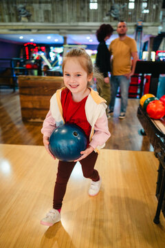 Little girl holding an orange ball at bowling in indoor alley
