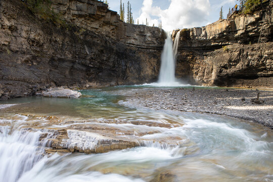 Majestic Waterfall Cascading Into Rocky River Pool Below Cliff W